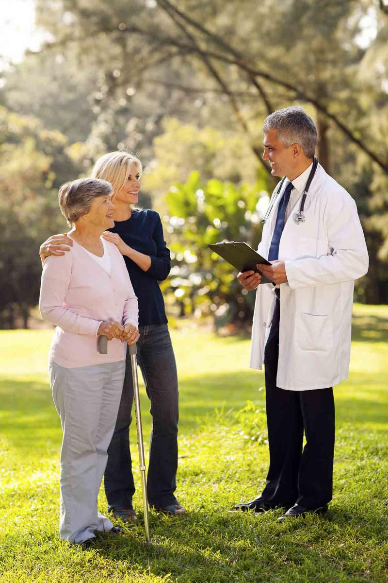 an older woman with her daughter stand outside with a male physician