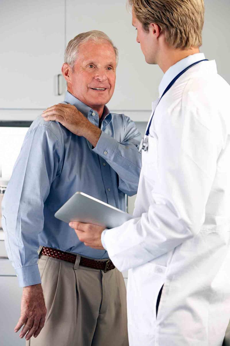 an older male patient shows a male physician the location of his shoulder pain