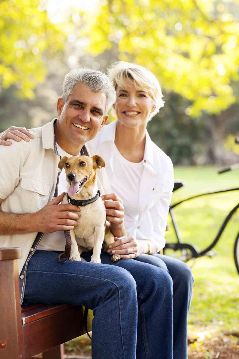 a smiling man and woman sitting outside with a small dog