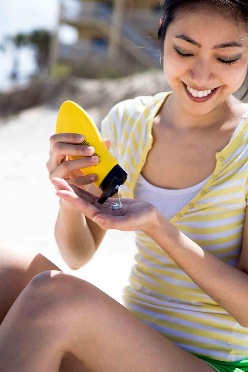 a young woman smiles as she applies sunscreen