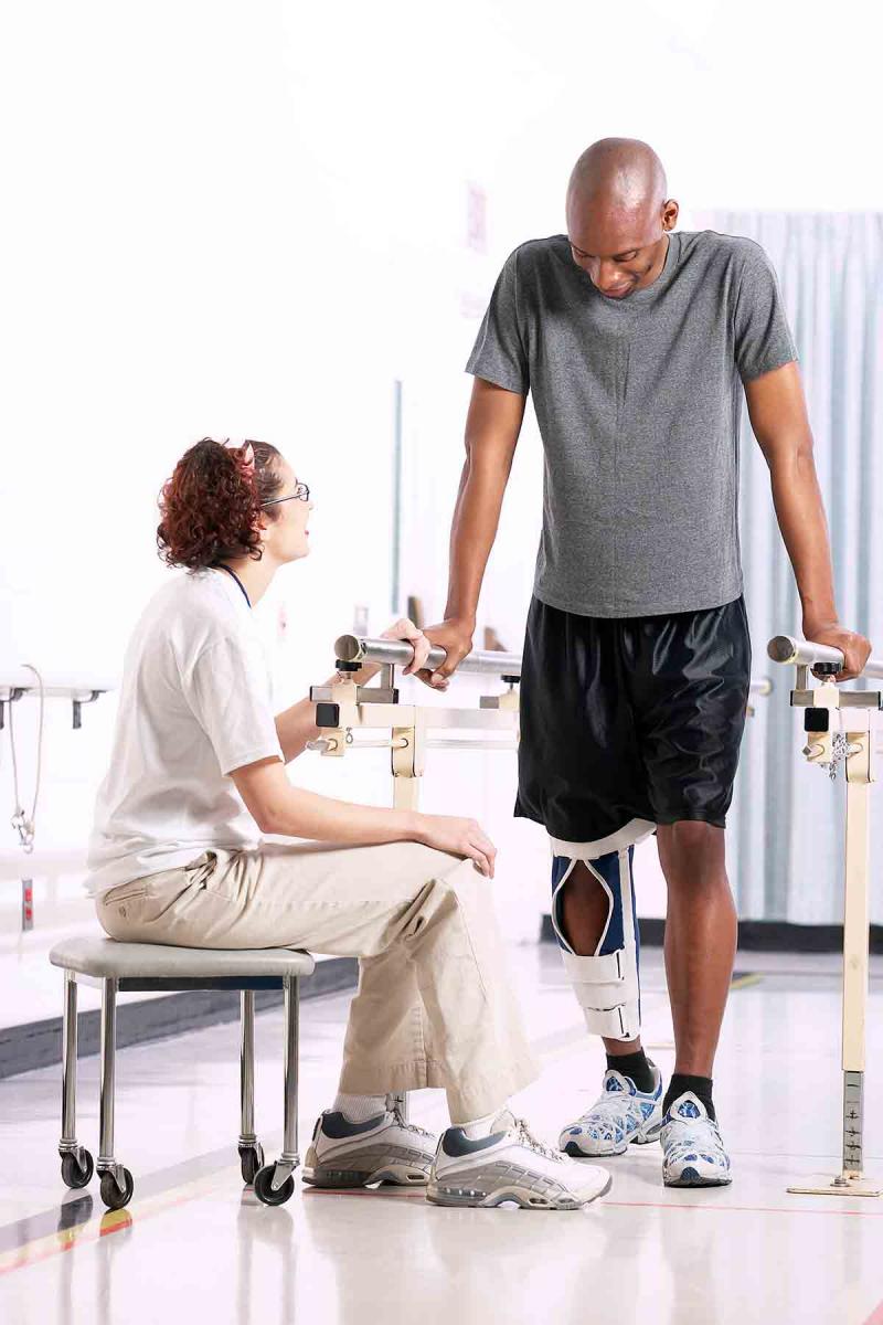 a man with a leg brace at physical therapy, with a seated woman nearby