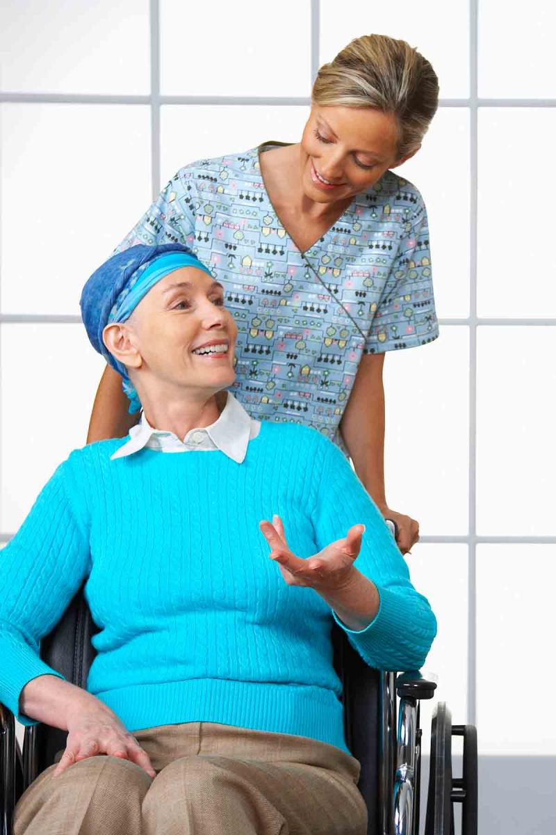 a female cancer patient in a wheelchair speaks to her female nurse