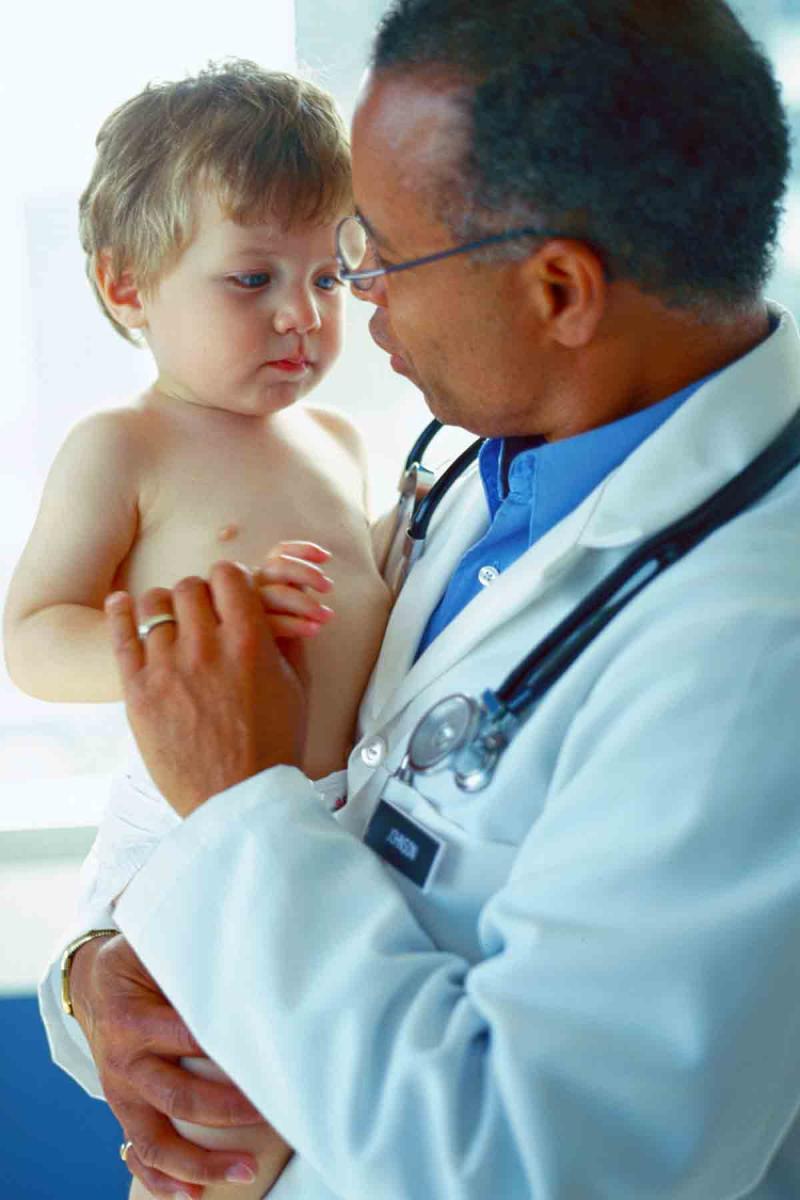 a male doctor holds and speaks to a young boy in a clinical setting